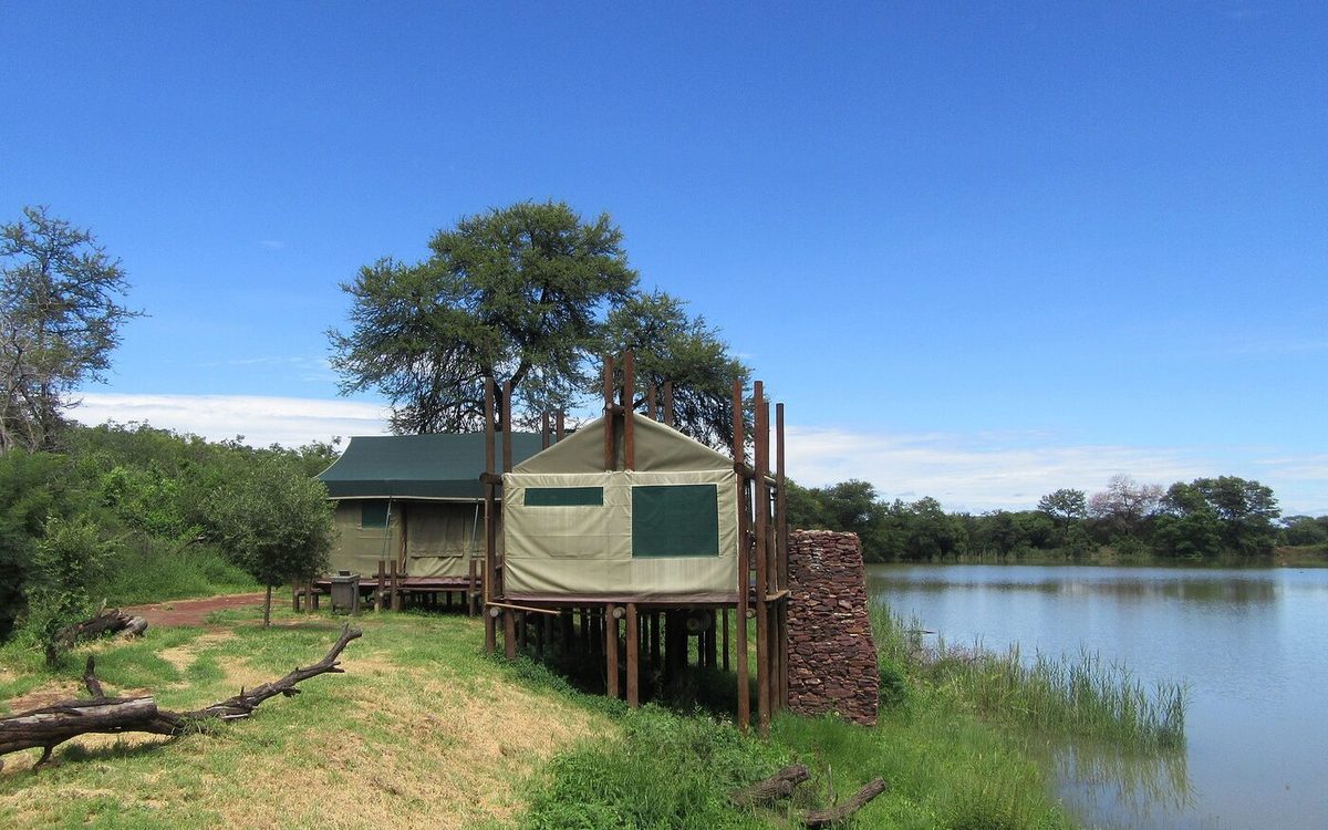 Tented safari camp raised on stilts overlooking a quiet waterway